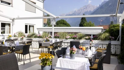 Terrasse eines Restaurants mit Tischen, Stühlen und Bergblick