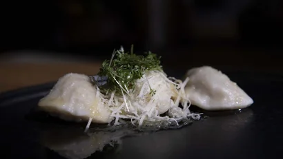 Drei Ravioli mit geriebenem Käse und frischen Kräutern auf dunklem Teller