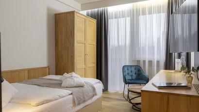 Modernes Schlafzimmer mit Holzmöbeln, blauem Sessel und großem Fenster mit Vorhängen