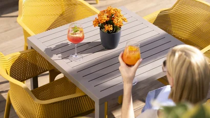 Frau mit Getränk an grauem Tisch und gelben Stühlen im Außenbereich