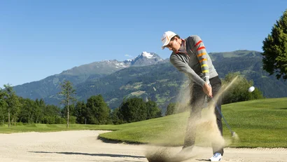 Golfer schlägt aus einem Bunker mit Bergkulisse im Hintergrund