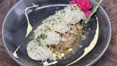 Gekochtes Gericht mit geriebenem Käse, Kräutern und essbarer Blume auf schwarzem Teller