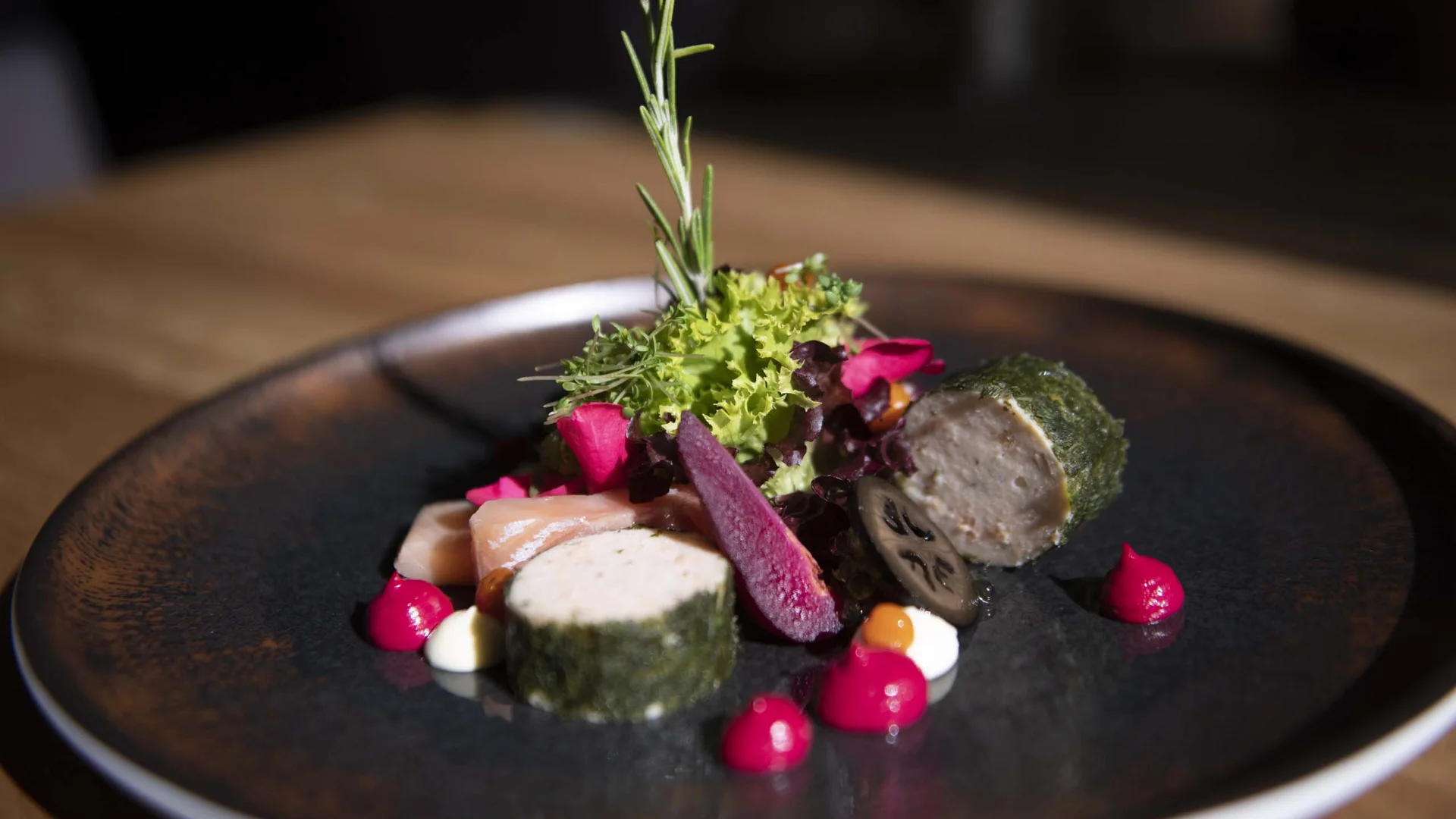 Fein angerichtetes Gericht mit Fisch und Garnierung auf dunklem Teller