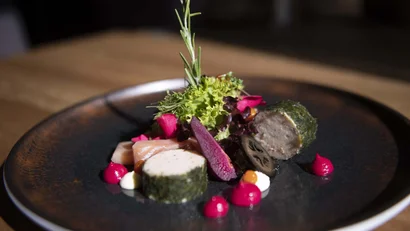 Fein angerichtetes Gericht mit Fisch und Garnierung auf dunklem Teller