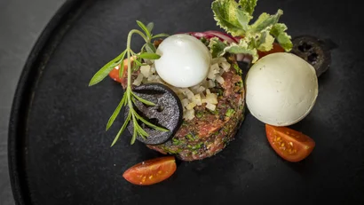 Steak Tatar mit Wachtelei, Oliven, Kräutern und Kirschtomaten auf schwarzem Teller