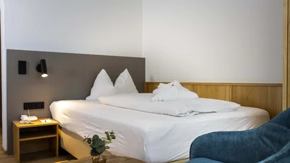 Modernes Hotelzimmer mit Doppelbett, Nachttisch, Leselampe und blauem Sessel
