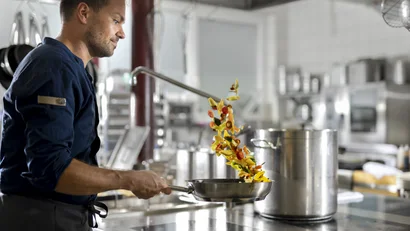 Mann kocht und wirft Gemüse in einer Pfanne in einer professionellen Küche