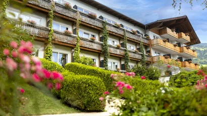 Haus mit Holzbalkonen und blühenden Pflanzen vor blauem Himmel