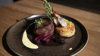 Gourmetgericht mit Rinderfilet, Garnelen, Kräutern und Kartoffelgratin auf dunklem Teller