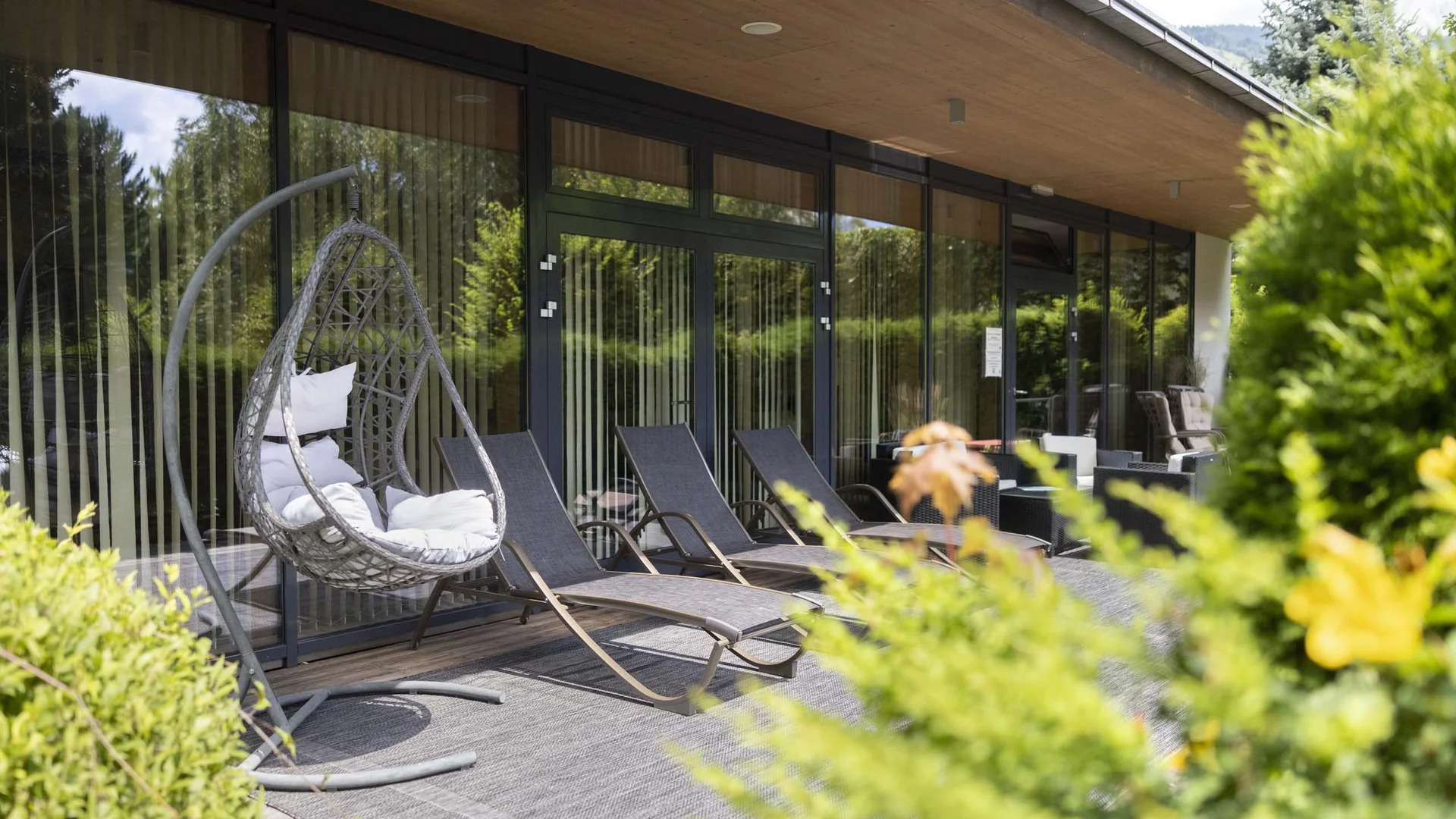 Terrasse mit Hängesessel und Liegestühlen vor Glaswand