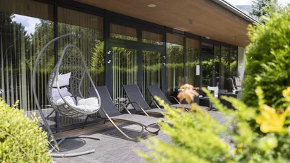 Terrasse mit Hängesessel und Liegestühlen vor Glaswand