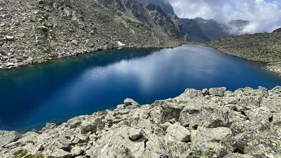 Blauer Bergsee umgeben von Felsen und bewölktem Himmel