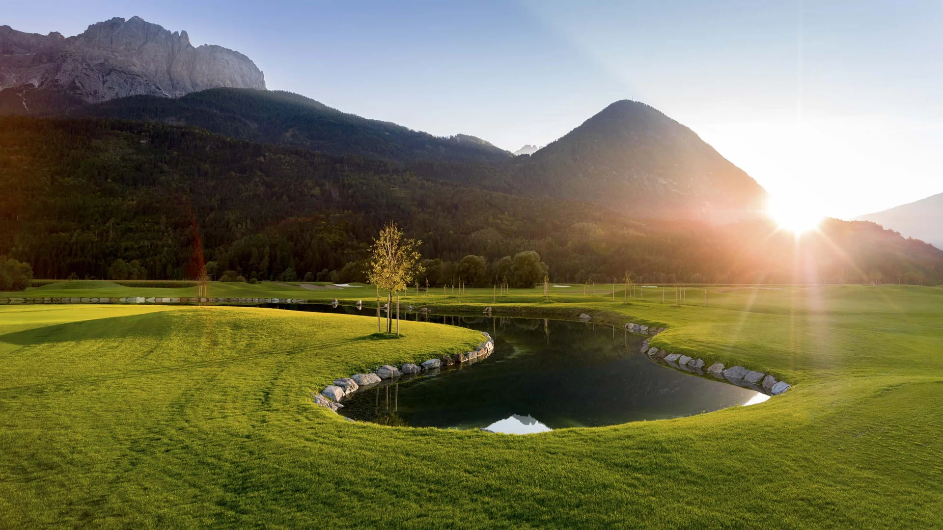 Golfplatz mit Teich und Bergen bei Sonnenaufgang