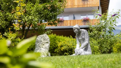 Skulptur einer knieenden Frau im Garten vor einem Haus mit Balkon