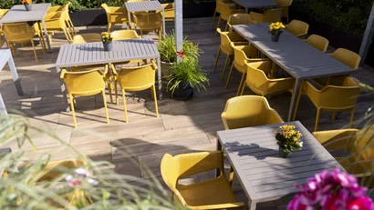 Leerer Außenbereich eines Cafés mit gelben Stühlen und grauen Tischen
