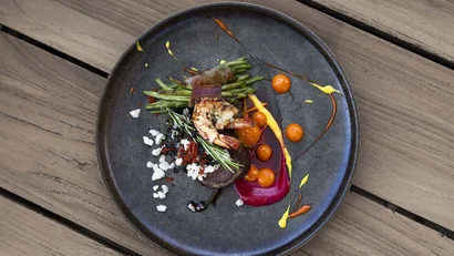 Gourmetgericht mit Garnele, grünem Gemüse und verschiedenen Saucen auf schwarzem Teller