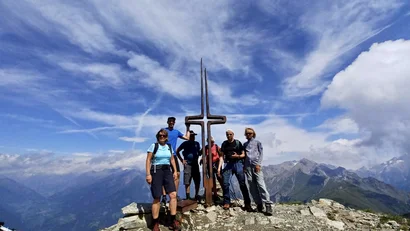 Gruppe von Wanderern am Gipfelkreuz mit Bergpanorama und blauem Himmel
