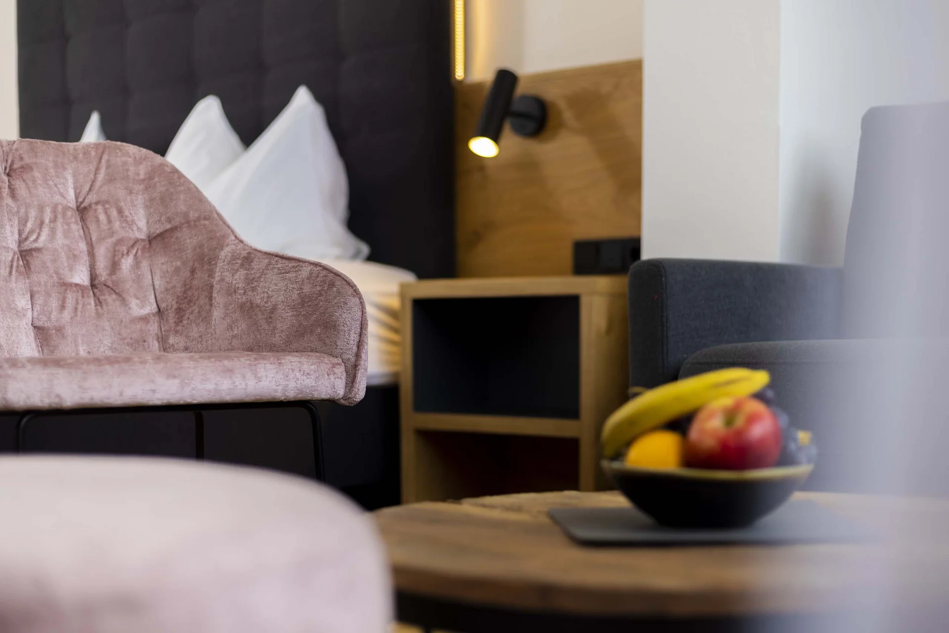 Modernes Hotelzimmer mit samtrosa Stuhl und Obstschale auf Holztisch