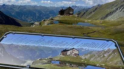Bergpanorama mit beschrifteten Gipfeln und Almhütte bei klarem Himmel