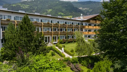 Hotel mit Garten und Bergen im Hintergrund unter bewölktem Himmel