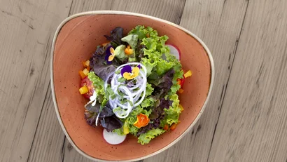 Bunter Salat mit Blüten in einem braunen Schüssel auf Holztisch
