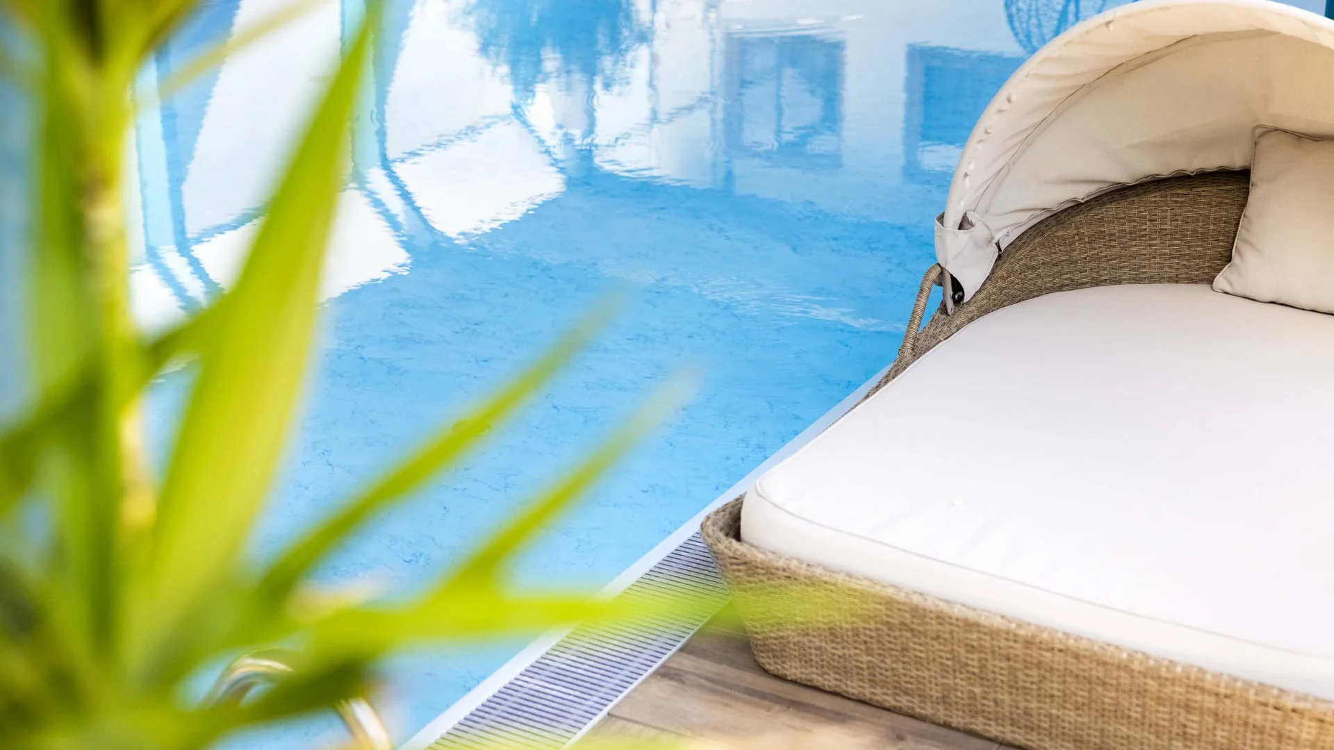 Liege mit Polster neben klarem blauen Pool und grüner Pflanze
