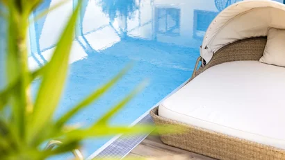 Liege mit Polster neben klarem blauen Pool und grüner Pflanze