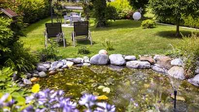 Garten mit Teich, zwei Liegestühlen und Sitzbereich bei Sonnenschein