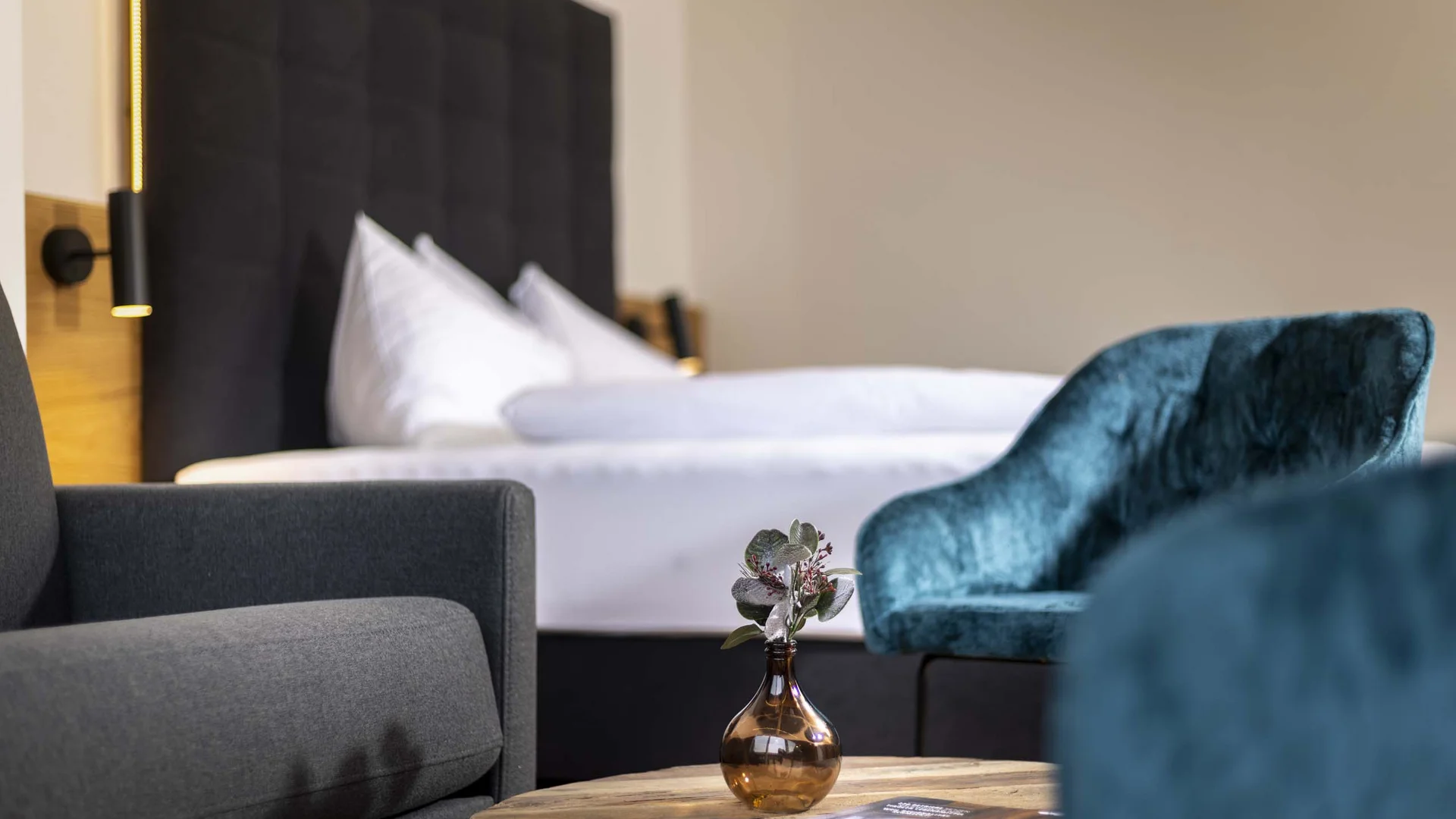 Gemütliche Hotelsuite mit Couch, Sessel, Bett und Holztisch mit Vase