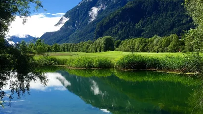 Berglandschaft mit See, bewaldeten Hügeln und blauem Himmel