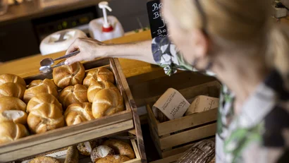 Frau nimmt Brötchen aus Holzkiste in Bäckerei mit Zange